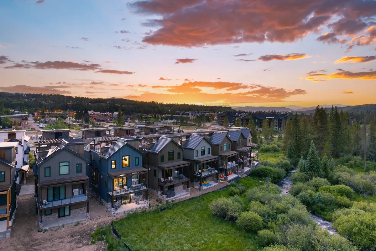 This exterior shot captures a row of modern townhouses set against a serene backdrop of lush greenery and a gently flowing stream, with a golden sunset illuminating the landscape. Walking and biking paths meander alongside the homes, inviting residents to enjoy the outdoors and the peaceful atmosphere.