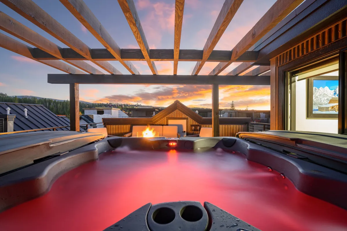 An outdoor area featuring a hot tub, a glowing fire pit, and a beautiful sunset sky. The space feels tranquil and intimate, perfect for relaxing after a day of urban and outdoor adventures.