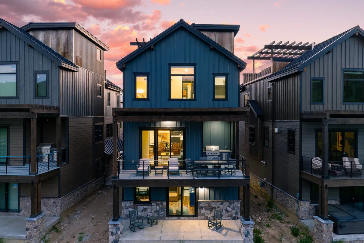 A welcoming view of the villa's blue exterior, featuring large windows, a spacious deck with seating, and surrounding homes that hint at a vibrant yet peaceful community. The deck is designed for outdoor dining or relaxation, blending comfort and connection to the landscape.
