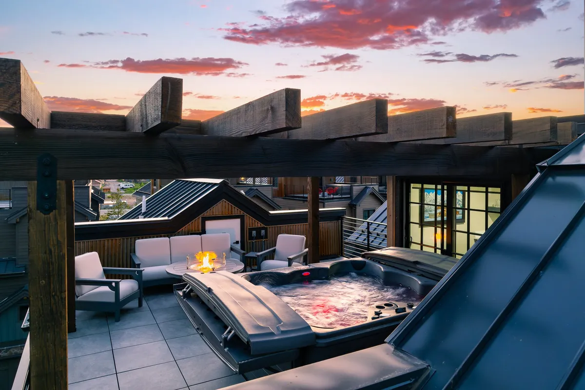 A close-up exterior shot showcases a hot tub and cozy fire pit surrounded by inviting seating. The backdrop includes mountains, with a dreamy evening sky hinting at stargazing opportunities. The ambiance is both romantic and tranquil, perfect for après-ski or evening relaxation.