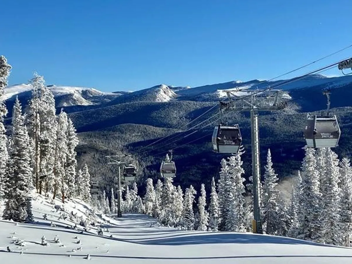 An exterior shot capturing ski lift gondolas ascending over a snowy landscape, surrounded by snow-laden trees and backed by a majestic mountain range. The scene is tranquil yet adventurous, evoking the spirit of winter sports.