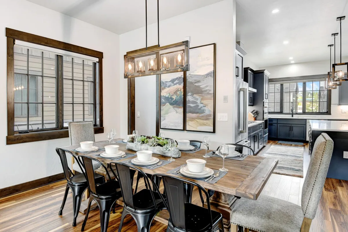 An elegant dining area with a custom wood table, chandelier, wall art, and windows that bring in soft daylight. The setup is perfect for celebratory meals or sharing stories with loved ones.