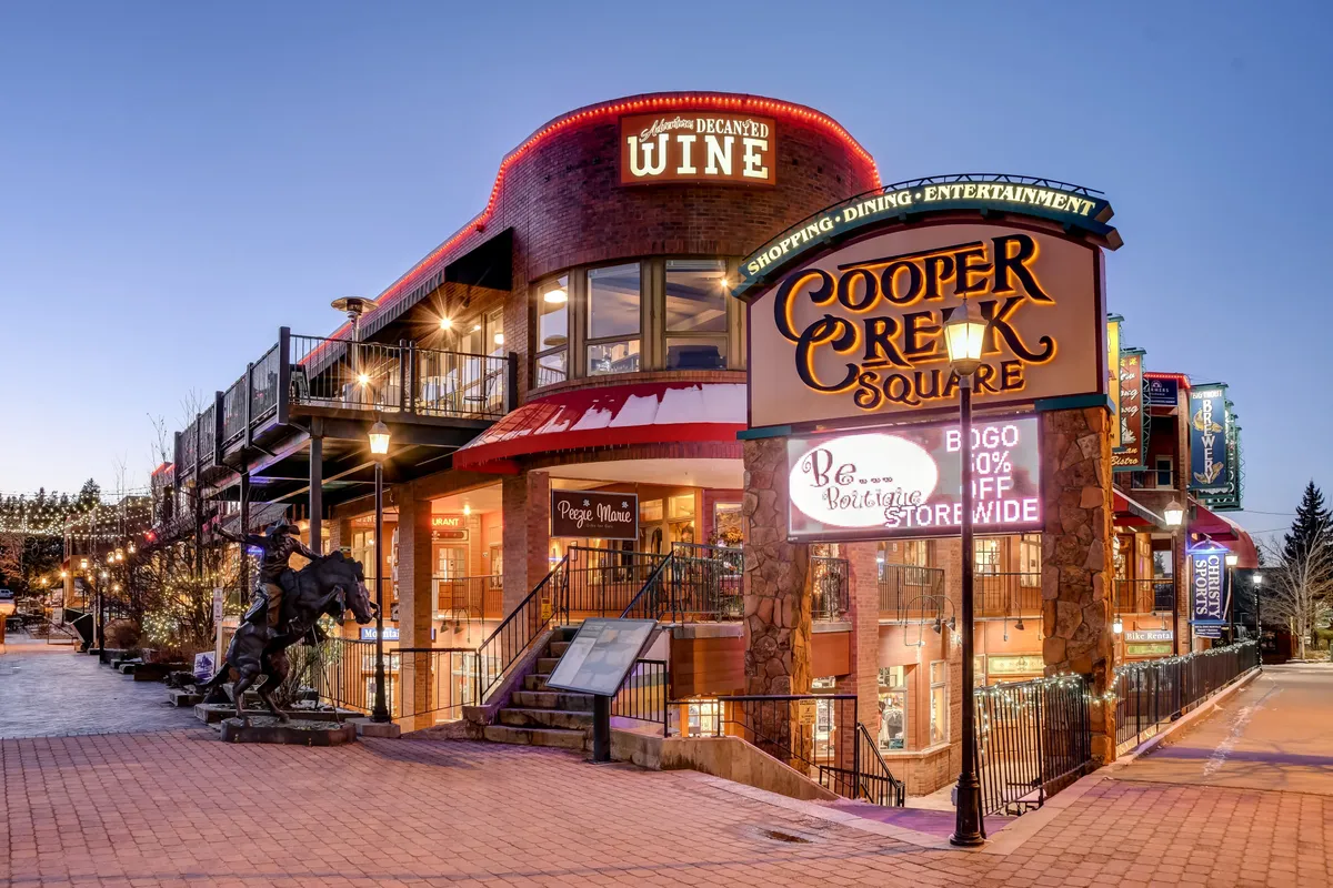 This lively exterior image captures Cooper Creek Square, with its wine shop entrance, festive exterior lighting, and decorative elements on the buildings. The scene is bustling, hinting at the shopping, dining, and live entertainment experiences available within walking distance from the villa.