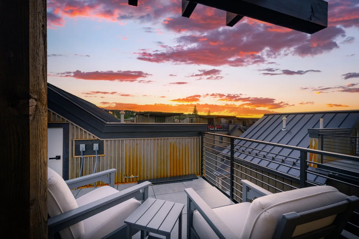 An exterior rooftop view with two armchairs and a small table, overlooking a sunset sky and distant landscape. The scene is tranquil and inviting, designed for relaxation and intimate gatherings while enjoying beautiful views.